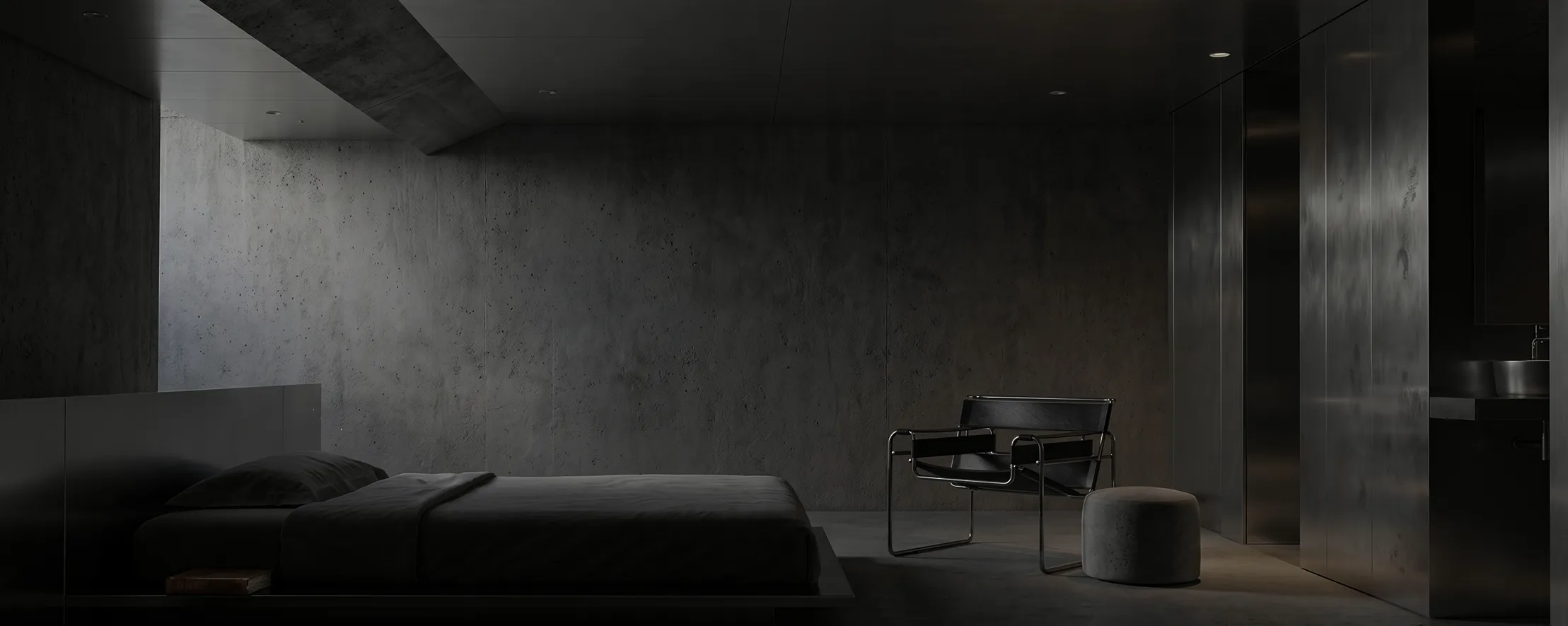 Dark minimalist bedroom with a low bed, black metal chair, round ottoman, and concrete walls.